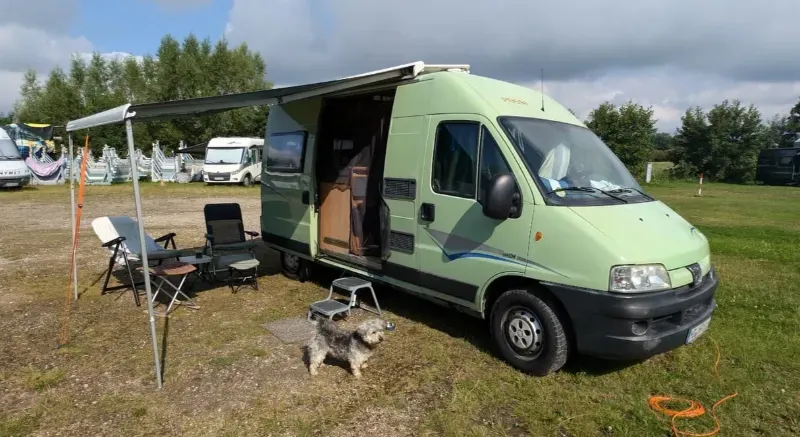 Grünes Kastenwagen-Wohnmobil mit Markise und Hund davor – Beispiel eines gebrauchten Wohnmobils für den Ankauf
